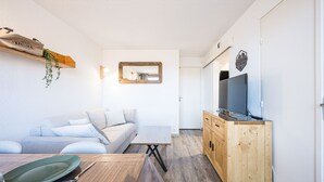 Een moderne woonkamer met een houten eettafel, een bank en een televisie op een houten kast.