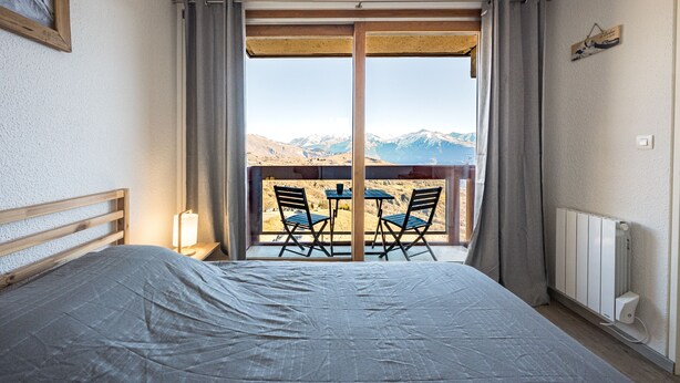 Een slaapkamer met een groot bed, een nachtkastje, een tafel met stoelen en uitzicht op bergen door een schuifdeur.