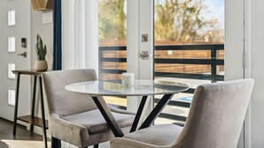 A modern room with a glass table and two chairs, a potted plant, and a view of a wooden deck and trees. - Cozy 1-bedroom condo in charming Fort Worth (Fort Worth)