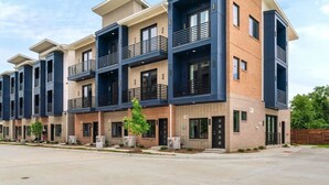 A modern multi-story residential building with balconies, brick facade, and a clear sky. - Cozy 1-bedroom condo in charming Fort Worth (Fort Worth)