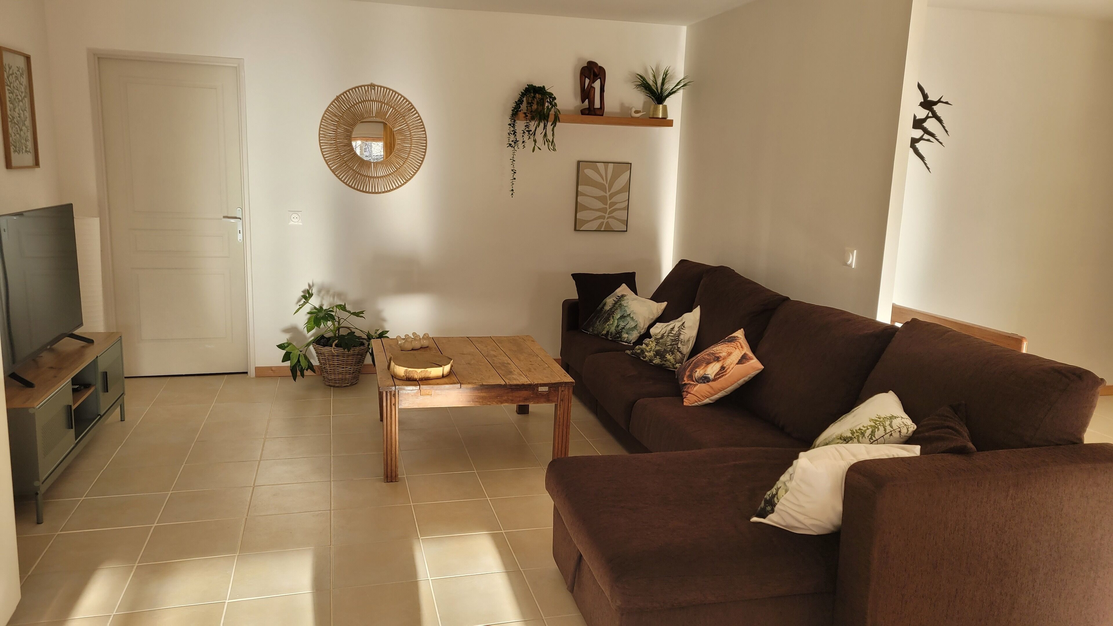 A living room with a brown sofa, a wooden coffee table, a TV on a stand, and a door.