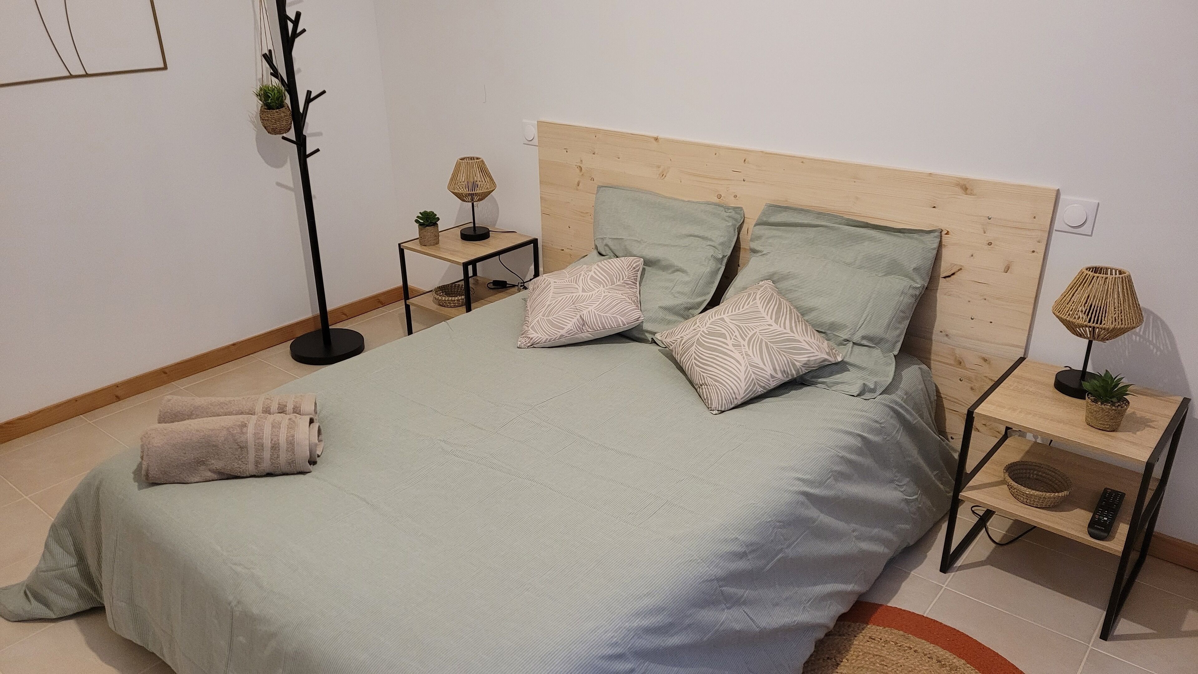 A neatly made bed with a wooden headboard, two bedside tables with lamps, and a small potted plant on one table.