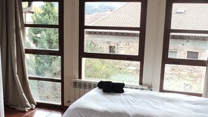 Une chambre d’hôtel avec deux lits, un radiateur et une vue sur une cour intérieure bordée d’arbres et entourée de bâtiments.