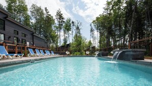 Ein Swimmingpool mit Liegestühlen, einem Wasserfall und einem Gebäude mit dunkler Fassade.