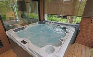 Un jacuzzi con panel de control, una ventana que da a zonas verdes y suelo de madera.