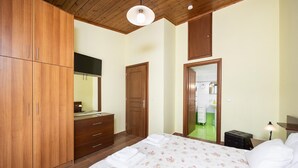 Un dormitorio con cama, armario de madera, un espejo y un baño visible a través de una puerta abierta.