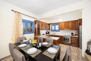 Una cocina moderna con armarios de madera, un comedor con una mesa dispuesta para cuatro personas y suelo de piedra.