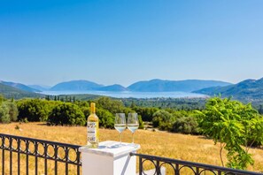 Une table avec une bouteille et des verres, donnant sur un paysage pittoresque avec des montagnes et des arbres.