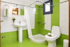 A bathroom with a shower, toilet, sink, and a window.