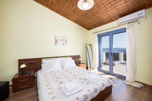 Une chambre avec un plafond en bois, un lit avec une literie à motifs floraux, une table de chevet, une lampe, une fenêtre avec des rideaux et un appareil de climatisation.