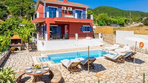 Una casa de dos pisos con piscina, mobiliario exterior y un patio de piedra.