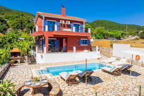 A two-story house with a swimming pool, outdoor furniture, and a stone patio.