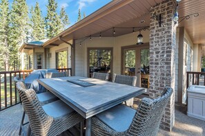 A covered patio with a dining table and wicker chairs, surrounded by a stone pillar and wooden beams.