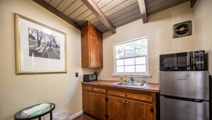 A kitchen with wooden cabinets, a stainless steel refrigerator, a microwave, and a window with a view of trees.