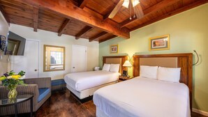 A hotel room with two beds, a wooden ceiling, and a small seating area with a table and chair.