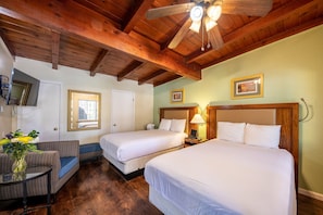 A hotel room with two beds, a wooden ceiling, and a small seating area with a table and chair.