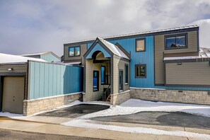 Un edificio residencial con garaje, un porche cubierto y un camino de entrada cubierto de nieve.