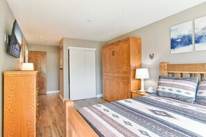 A bedroom with a bed, wooden wardrobe, a nightstand with a lamp, a television on the wall, and a door leading to another room. - Views of Lake Dillon and surrounding mountains! Lake Forest Condo (Frisco)