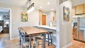 A modern kitchen with a wooden dining table, stainless steel appliances, and artwork on the walls. - Ski • Paddle • Hike | Lake Dillon | Hot Tub (Frisco)