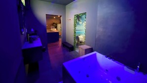 A spa area with a large bathtub, a small seating area with a bench, and a wall with a tropical mural. - Your Wellness Break! (Dalhem)
