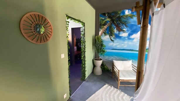 A room with a view of the beach, a wooden wall decor, a potted plant, and a white bed. - Your Wellness Break! (Dalhem)