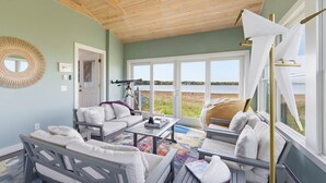 Una stanza con soffitto in legno, un'ampia finestra vista spiaggia, un divano bianco, un tavolino e una sedia.