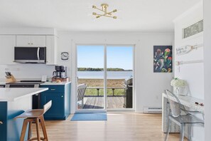 A modern kitchen with a large window, a dining area with a view, and a deck with a grill. - Wonderland on the Water with Exclusive Beach Access (Biddeford)