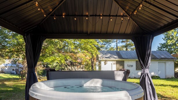Un jacuzzi bajo una zona cubierta con techo de madera y luces colgantes.
