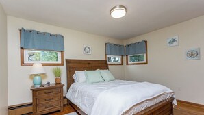 Un dormitorio con una cama de madera, una mesita de noche con lámpara y una ventana con cortinas azules.