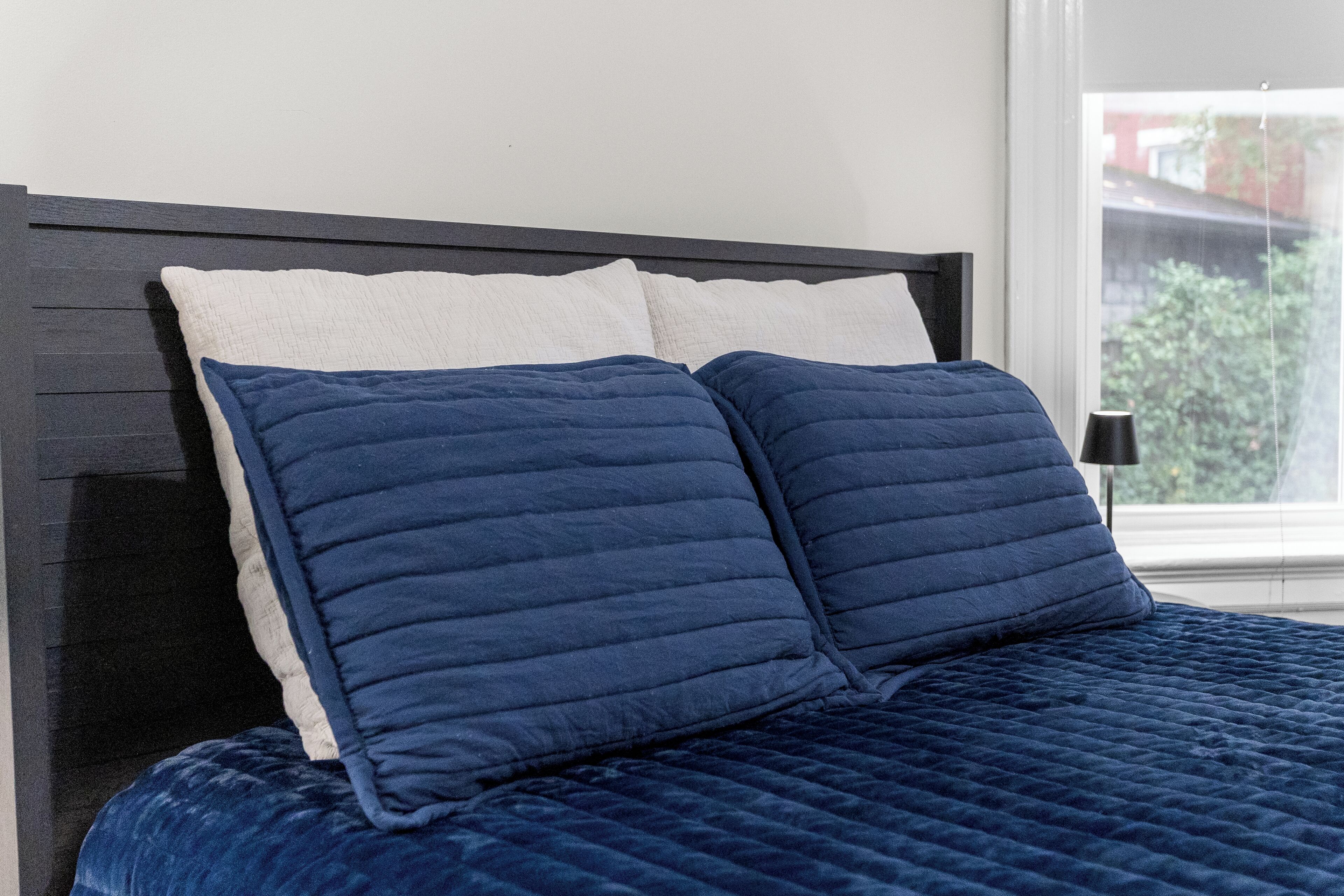 Un lit recouvert d’une courtepointe bleu foncé et orné de deux oreillers, un blanc et l’autre bleu foncé, adossé à une tête de lit sombre.