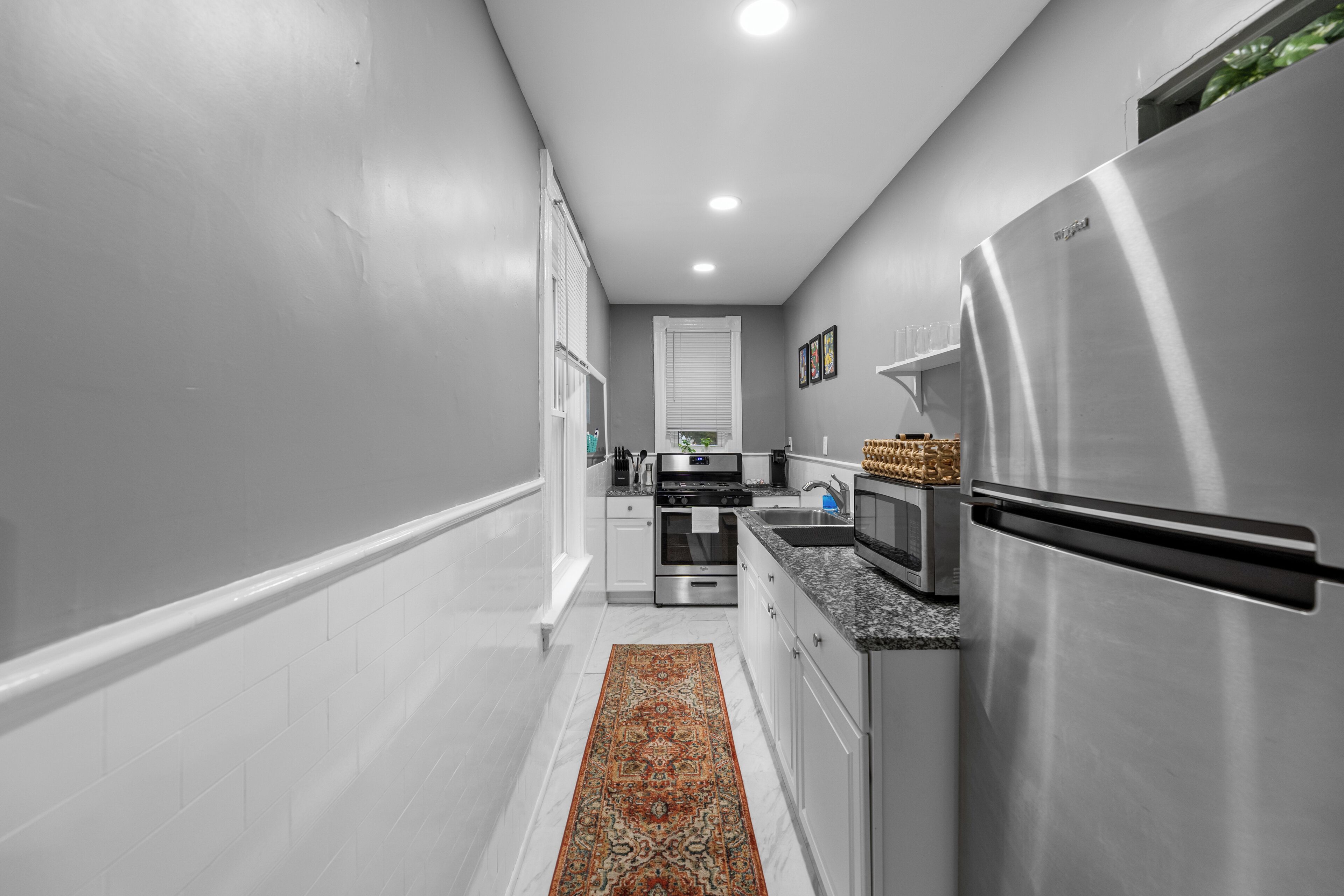 Una cucina moderna con mobili bianchi, elettrodomestici in acciaio inossidabile e un tappeto decorato.