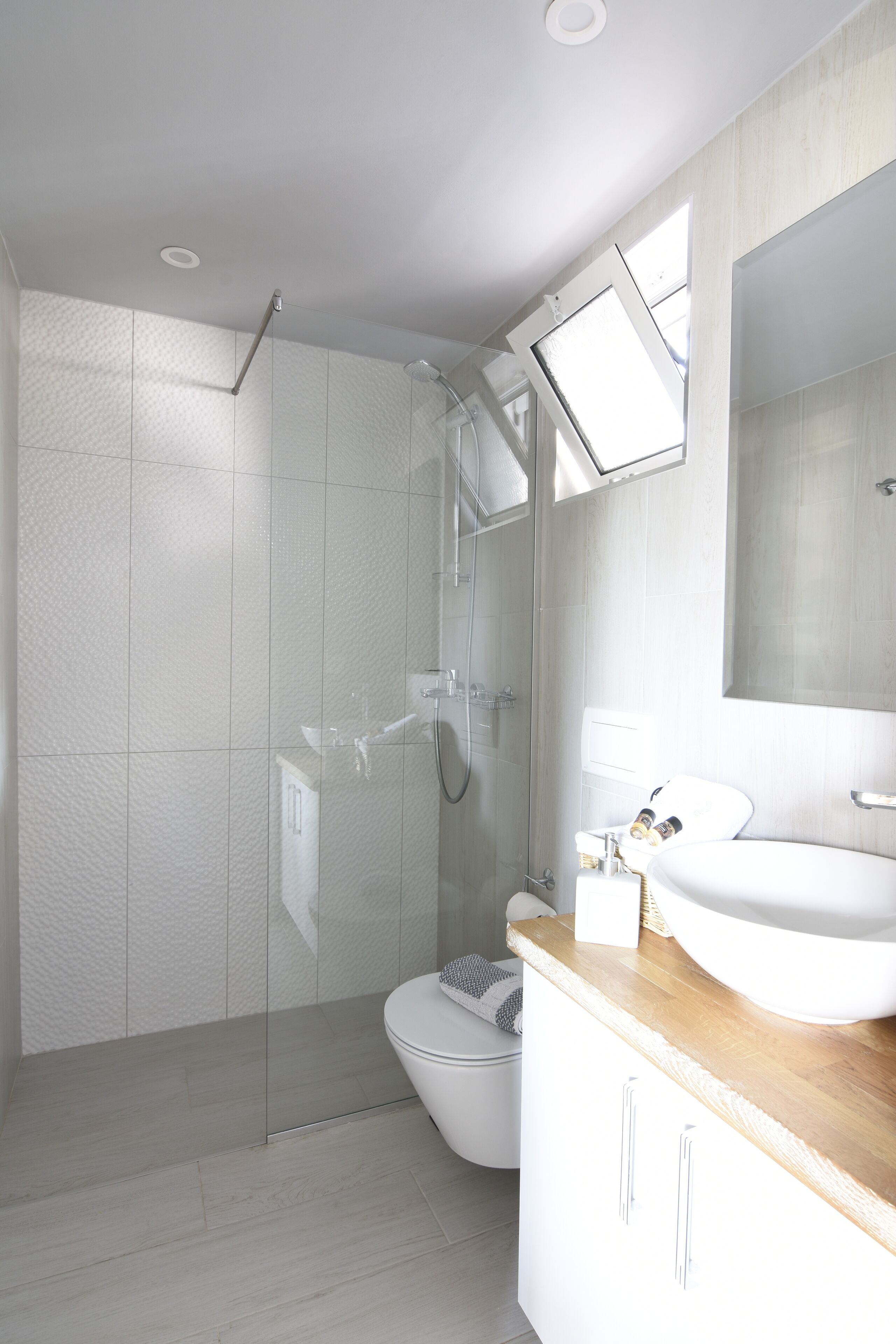 Een moderne badkamer met een douchecabine van glas, een wit toilet en een houten wastafelmeubel met een grote spiegel.