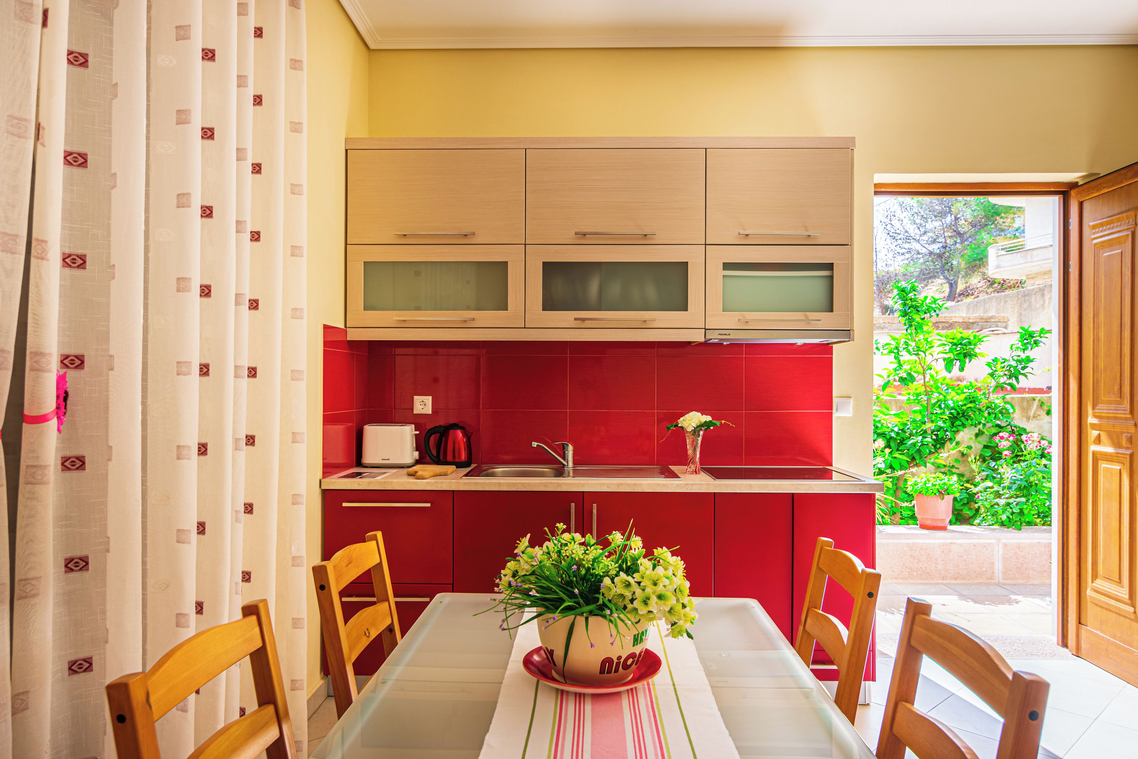 Una cocina compacta con armarios rojos, una mesa de comedor con sillas y una planta en maceta sobre la mesa.