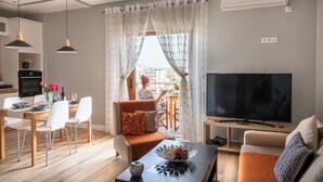 A modern living room with a TV, sofa, and dining area. - Great Alexander Suites (Sarande)