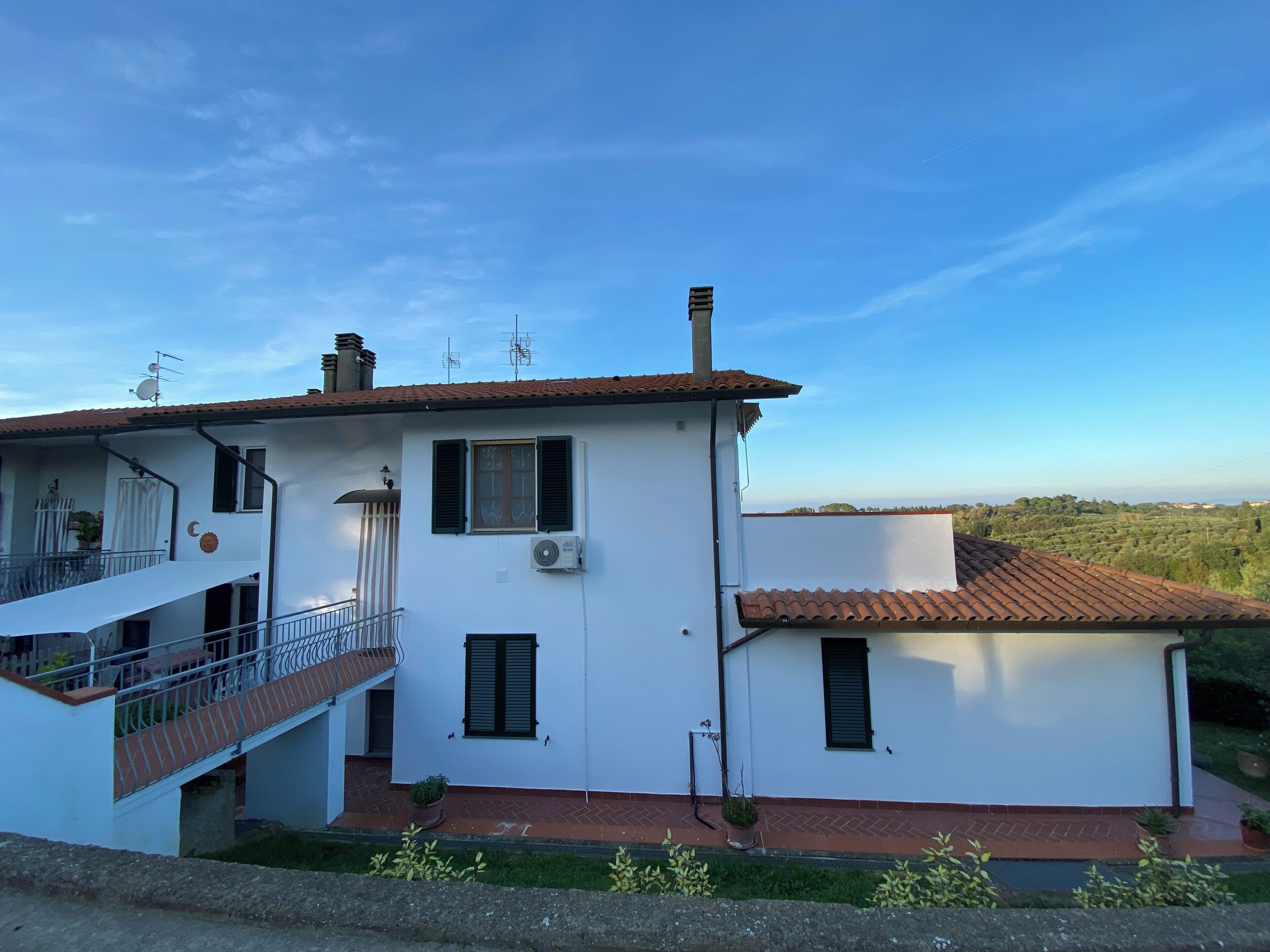 A two-story house with a balcony, a small garden, and a view of the countryside.