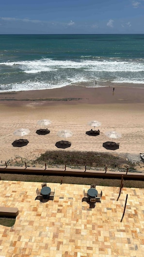 A beach with umbrellas and lounge chairs, a view of the ocean, and a tiled patio area. - Vila Porto Beira Mar (Ipojuca)