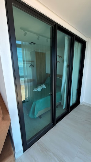 A modern bedroom with a glass door leading to a balcony, a bed with a green bedspread, and a wooden wardrobe. - Vila Porto Beira Mar (Ipojuca)