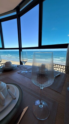 A table set with a white teapot, a cup, and a glass, overlooking a beach with the ocean visible through large windows. - Vila Porto Beira Mar (Ipojuca)
