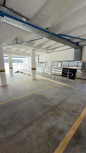 Ein Innenparkplatz mit Betonböden, weißen Säulen und blau-grünen Rohren an der Decke.