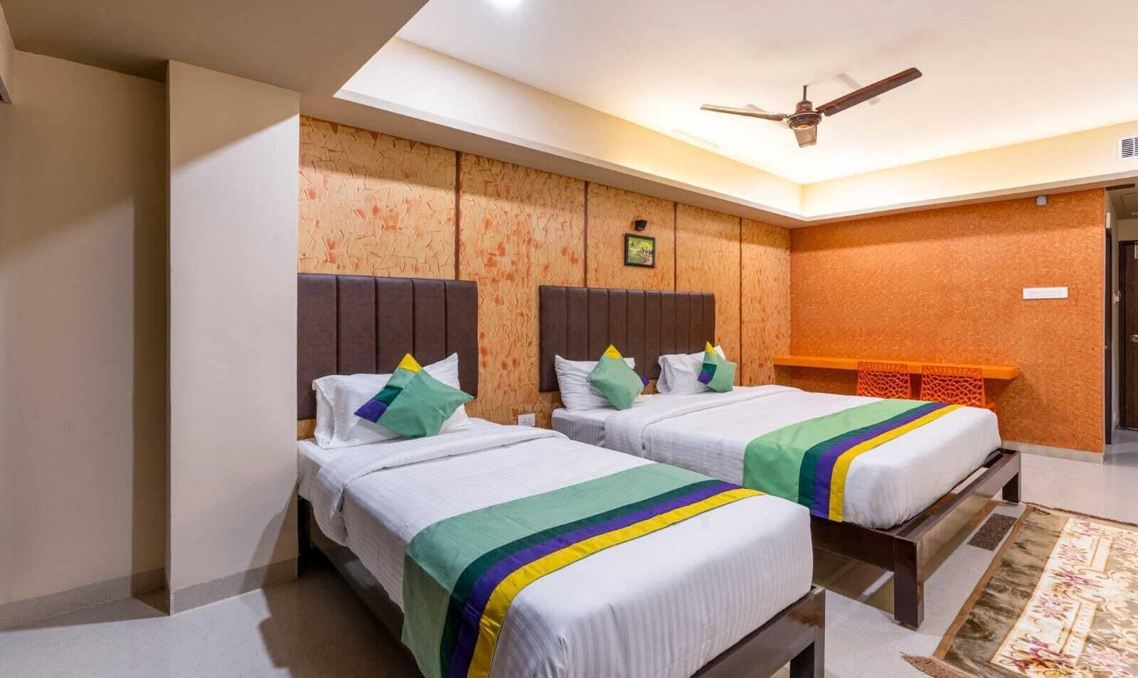 Una habitación de hotel con dos camas, un ventilador de techo y una pequeña zona de escritorio.