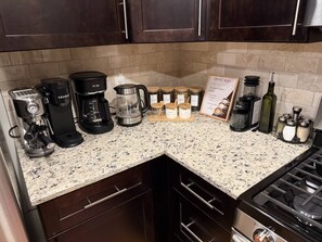 Eine Küche mit einer Kaffeemaschine, einer Kaffeekanne, einem Herd und verschiedenen Behältern auf der Arbeitsplatte.