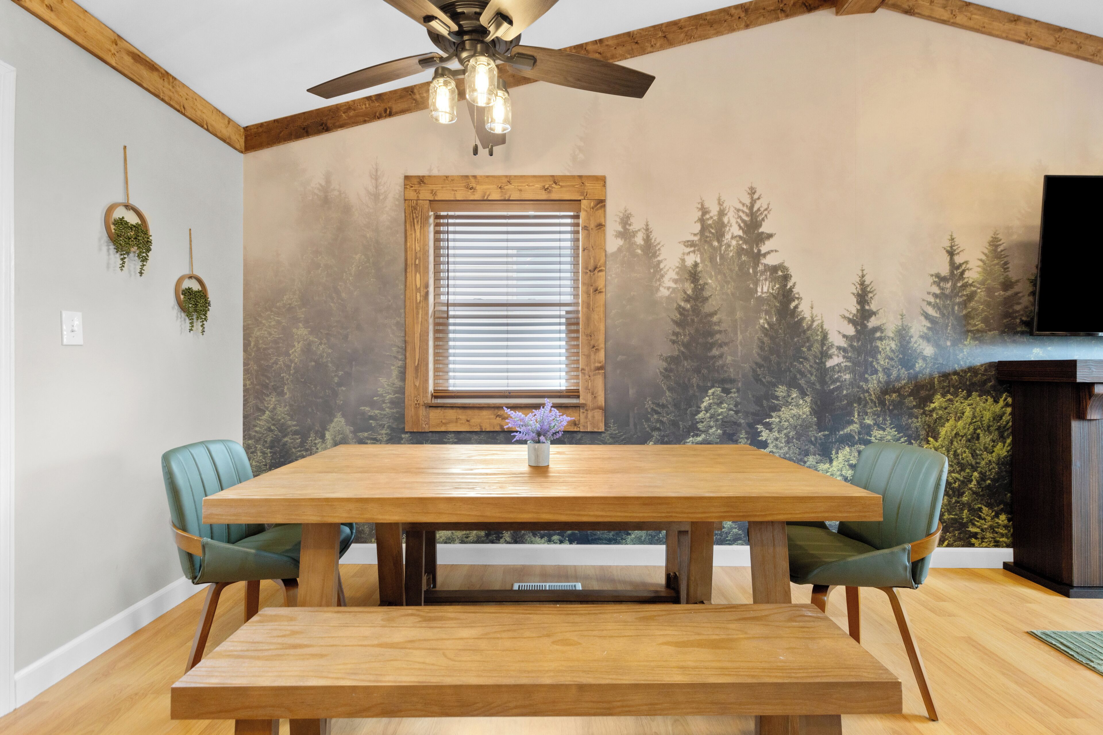 Un comedor con una mesa de madera, dos sillas, un ventilador de techo y una ventana con persianas.