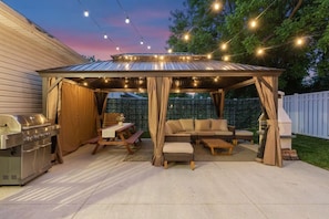 Eine überdachte Terrasse im Freien mit Grill, Sitzgelegenheiten und Lichterkette.