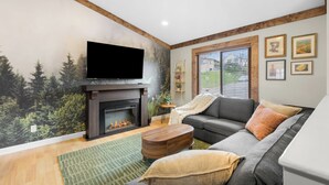 A living room with a fireplace, a flat-screen TV, a sofa, and a green rug. - Family Retreat w/ Hot Tub near Zoo & Forest Park (St. Louis)