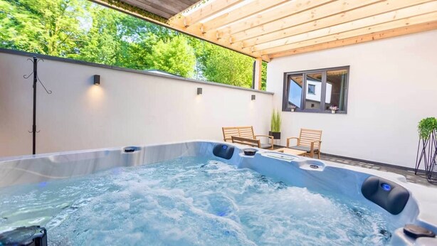 A hot tub area with a wooden pergola overhead, two wooden chairs, and a small table. - Charming 2-bedroom House Rental in Dalhem, Belgium (Dalhem)