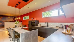 A modern kitchen with a central island, black appliances, and a red accent wall. - Charming 2-bedroom House Rental in Dalhem, Belgium (Dalhem)