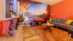 A modern living room with a large wall mural of a canyon, a sofa with cushions, a coffee table, and a colorful sculpture. - Charming 2-bedroom House Rental in Dalhem, Belgium (Dalhem)