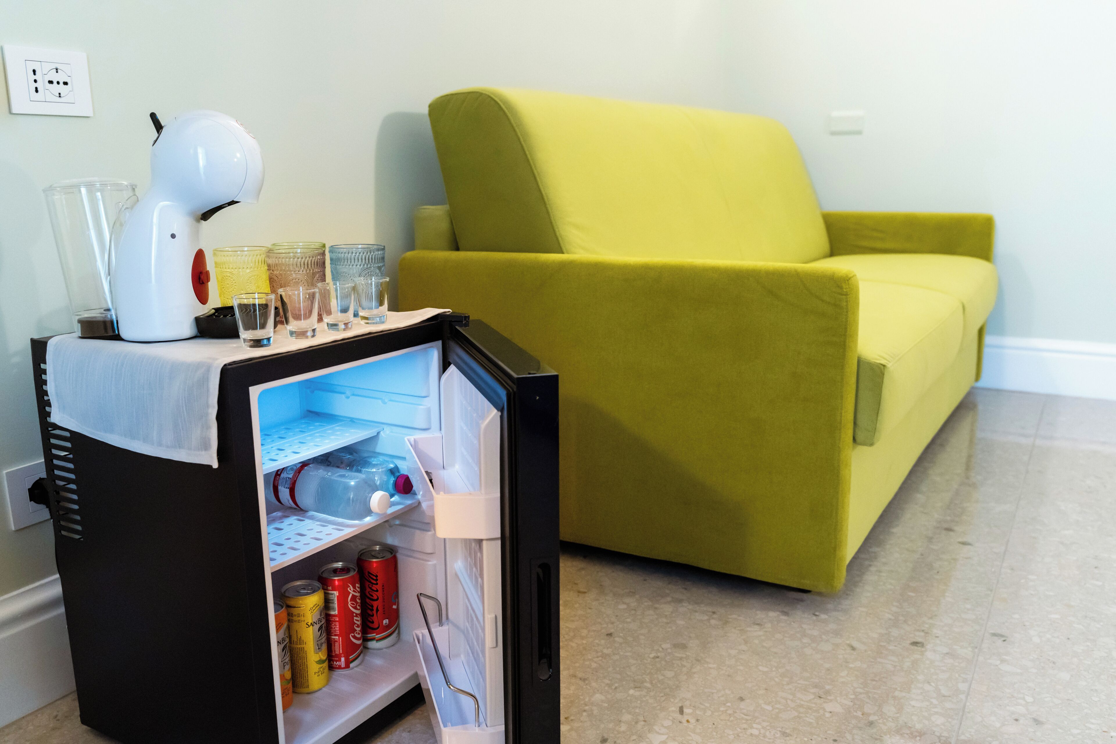 A compact kitchenette with a mini-fridge, a coffee maker, and a variety of glass containers.