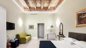 Una habitación de hotel con cama, sofá, televisor, un cuadro y una puerta.