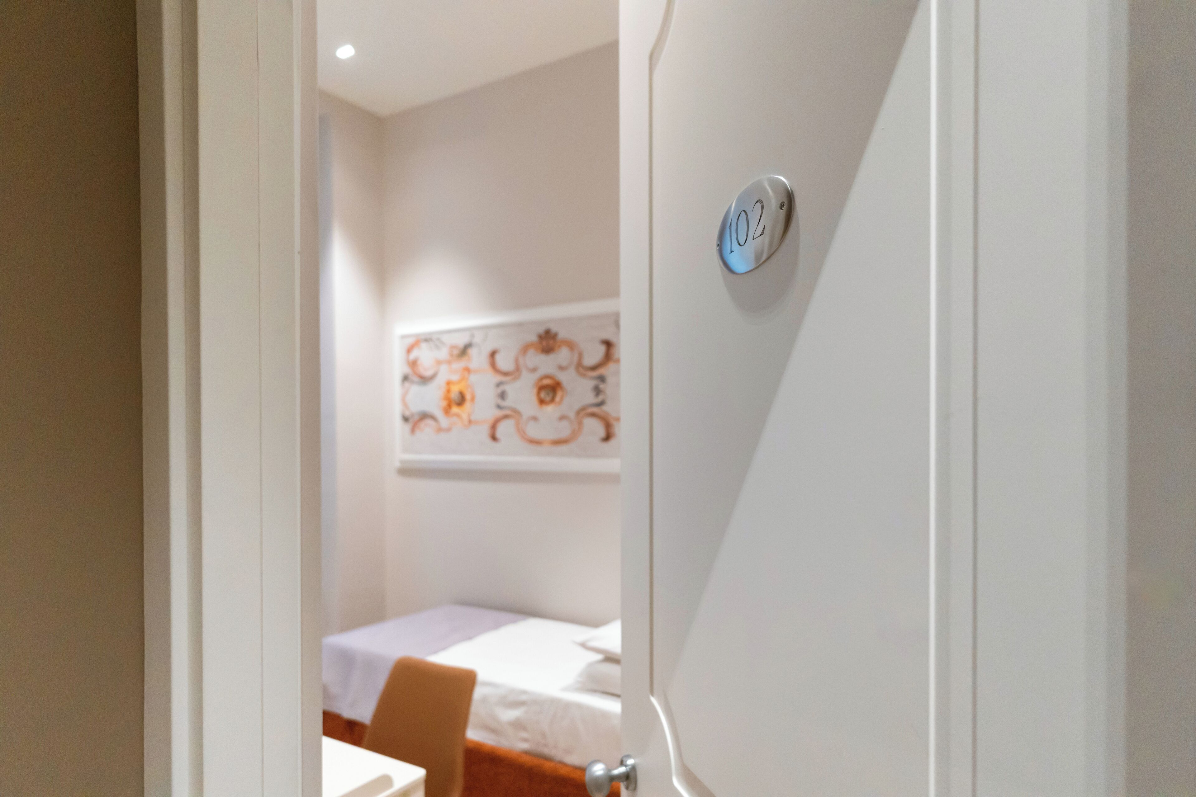 A hotel room with a bed, a chair, and a wall-mounted number plate.